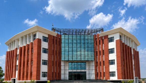 Modern university building with red brick pillars and a glass central atrium against a blue sky.