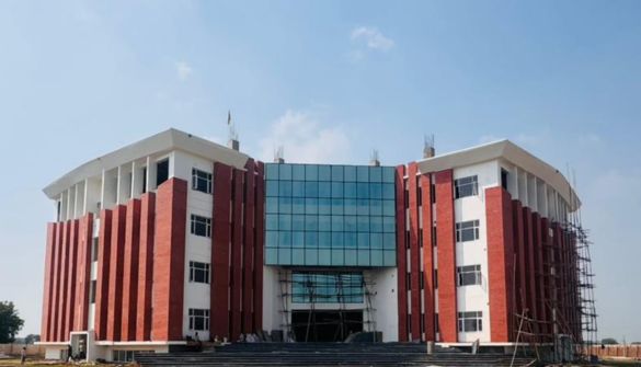 Seth M R Jaipuria School Agra - Jaipuria Schools - Jaipuria Schools Large modern building with red brick pillars and a blue glass facade under construction on a sunny day.