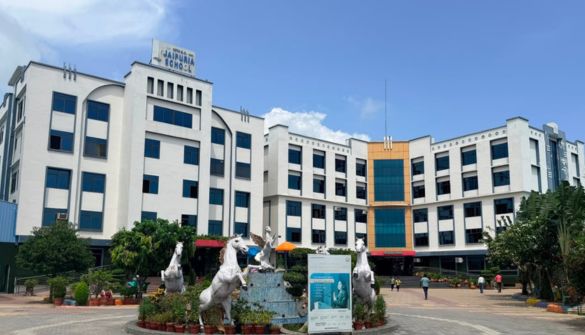 Seth M R Jaipuria School Azamgarh - Jaipuria Schools - Jaipuria Schools Front view of a white multi-story campus building with blue-tinted windows, a fountain with two white horse statues, and pedestrians in a courtyard.