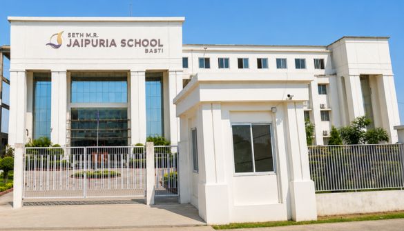 Seth M R Jaipuria School Basti - Jaipuria Schools - Jaipuria Schools Front entrance of Seth M.R. Jaipuria School Basti, a white modern building with tall columns, gate, and security booth under a blue sky.