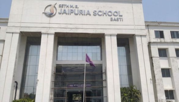 Front entrance of Seth M.R. Jaipuria School, Basti, with tall columns and a purple flag in front of glass doors.