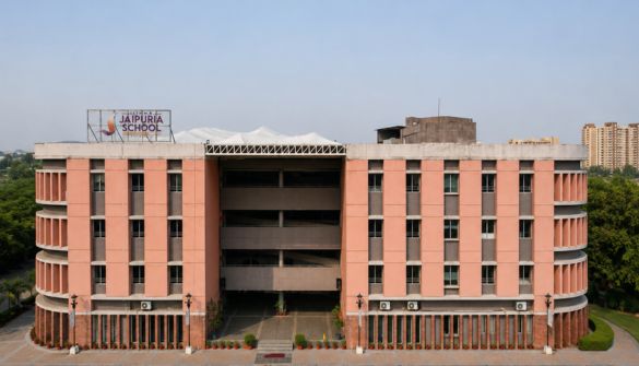 Seth M R Jaipuria School Bhiwadi - Jaipuria Schools - Jaipuria Schools Front view of a peach-colored school building with curved side wings, a central entrance, and a Jaipuria School sign on the roof.