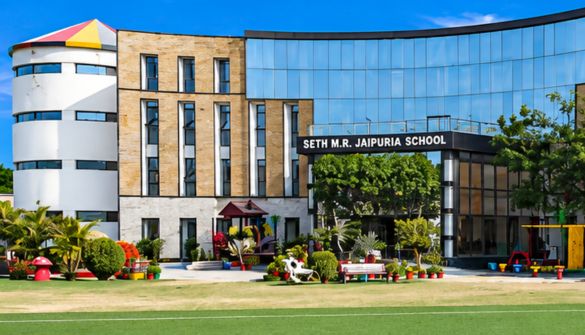 Front view of Seth M.R. Jaipuria School with a brick-and-glass facade and a colorful playground in the foreground.