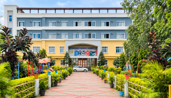 Seth M R Jaipuria School Gonda - Jaipuria Schools - Jaipuria Schools Front view of a blue-and-yellow school building with a central entrance, flanked by a landscaped walkway and potted plants.