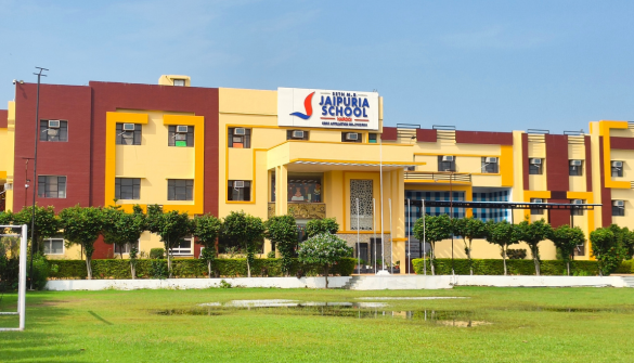 Seth M R Jaipuria School Hardoi - Jaipuria Schools - Jaipuria Schools Front facade of Jaipuria School, a colorful two-story building with yellow and maroon panels, a sign above the entrance, and a green lawn with trees in front.