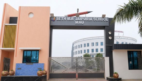 Seth M R Jaipuria School Mau - Jaipuria Schools - Jaipuria Schools Entrance gate of Seth M.R. Jaipuria School Mau, featuring a metal gate between peach and white buildings and a pencil sculpture on top.