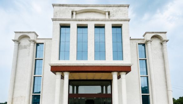 Seth M R Jaipuria School Mohanlalganj Lucknow - Jaipuria Schools - Jaipuria Schools Facade of a modern, light-colored building with tall blue-tinted windows and a covered entrance supported by columns.