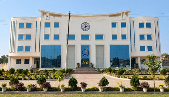 Front view of a large white, modern building with a central clock, blue glass windows, and a manicured front garden.