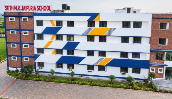 Facade of Seth M.R. Jaipuria School, a multi-story building with blue, white, and orange geometric stripes on the exterior.