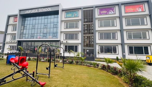 Seth M R Jaipuria School Sahaswan Campus - Jaipuria Schools - Jaipuria Schools Front view of Jaipuria School building with glass entrance and a playground in the lawn area in the foreground.